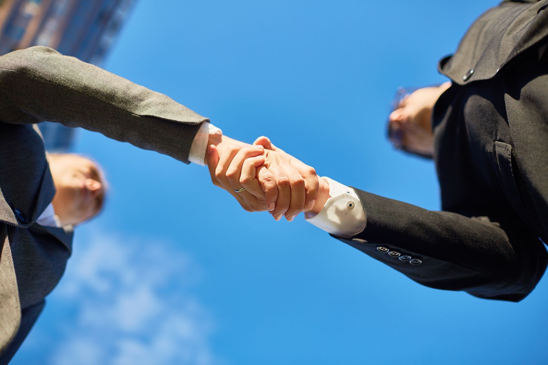 Two businessmen are shaking hands in front of a blue sky.