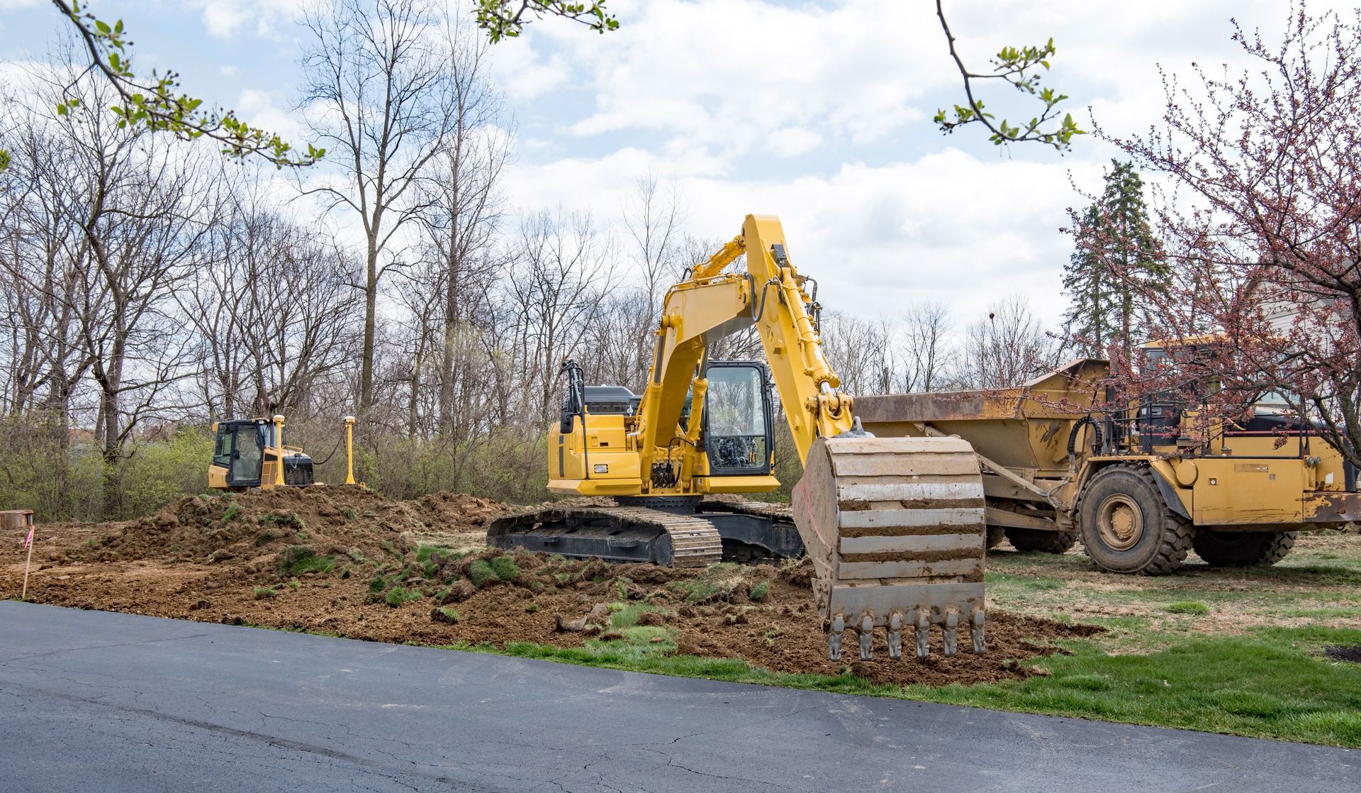 A yellow excavator is sitting on the side of a road next to a dump truck.