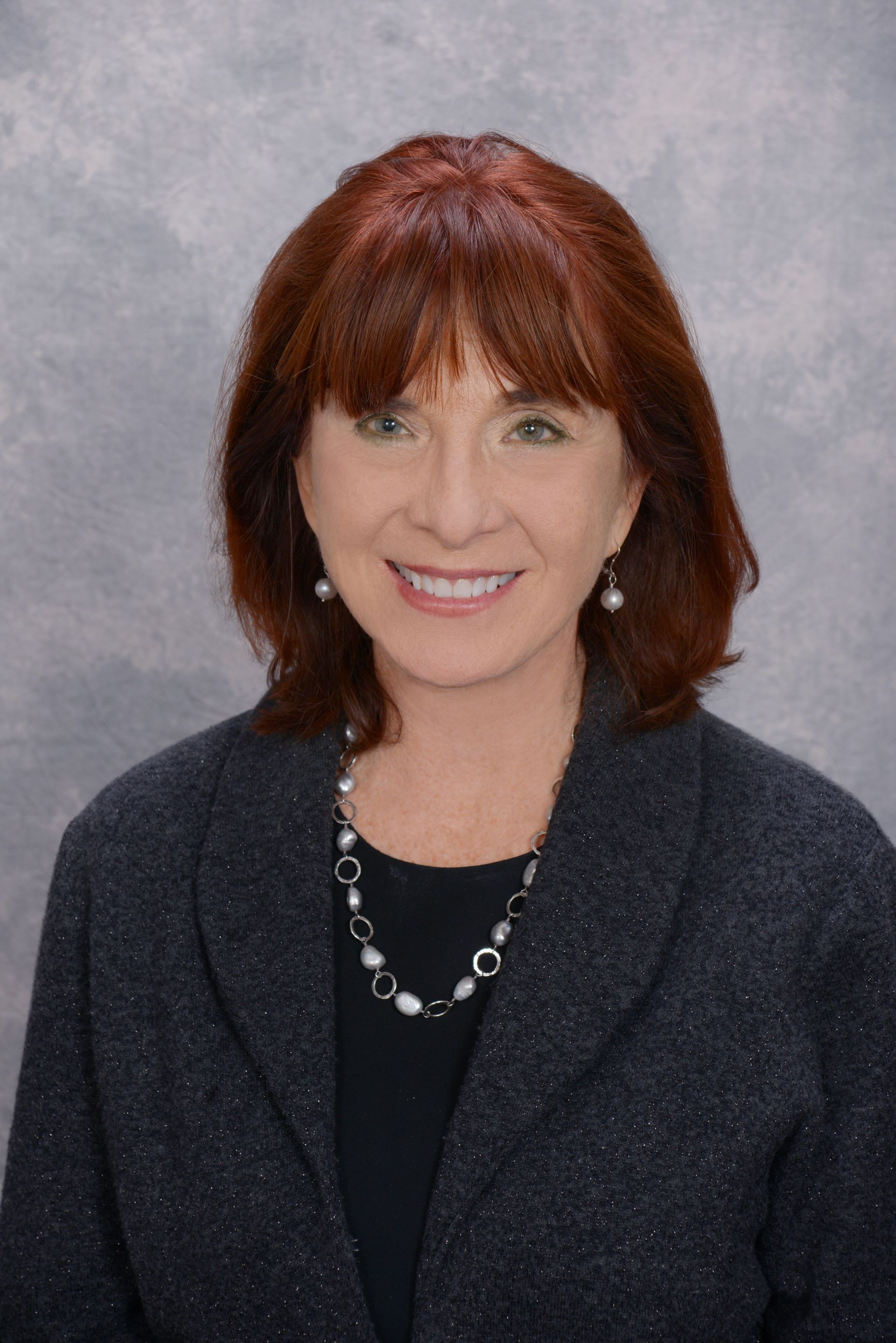 Red-haired woman in navy clothing. She is smiling.