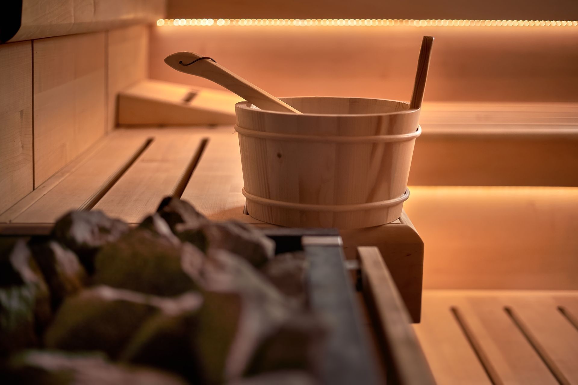 Sauna-Innenraum aus Holz mit Eimer, Schaufel und beheizten Steinen. Warme Beleuchtung.