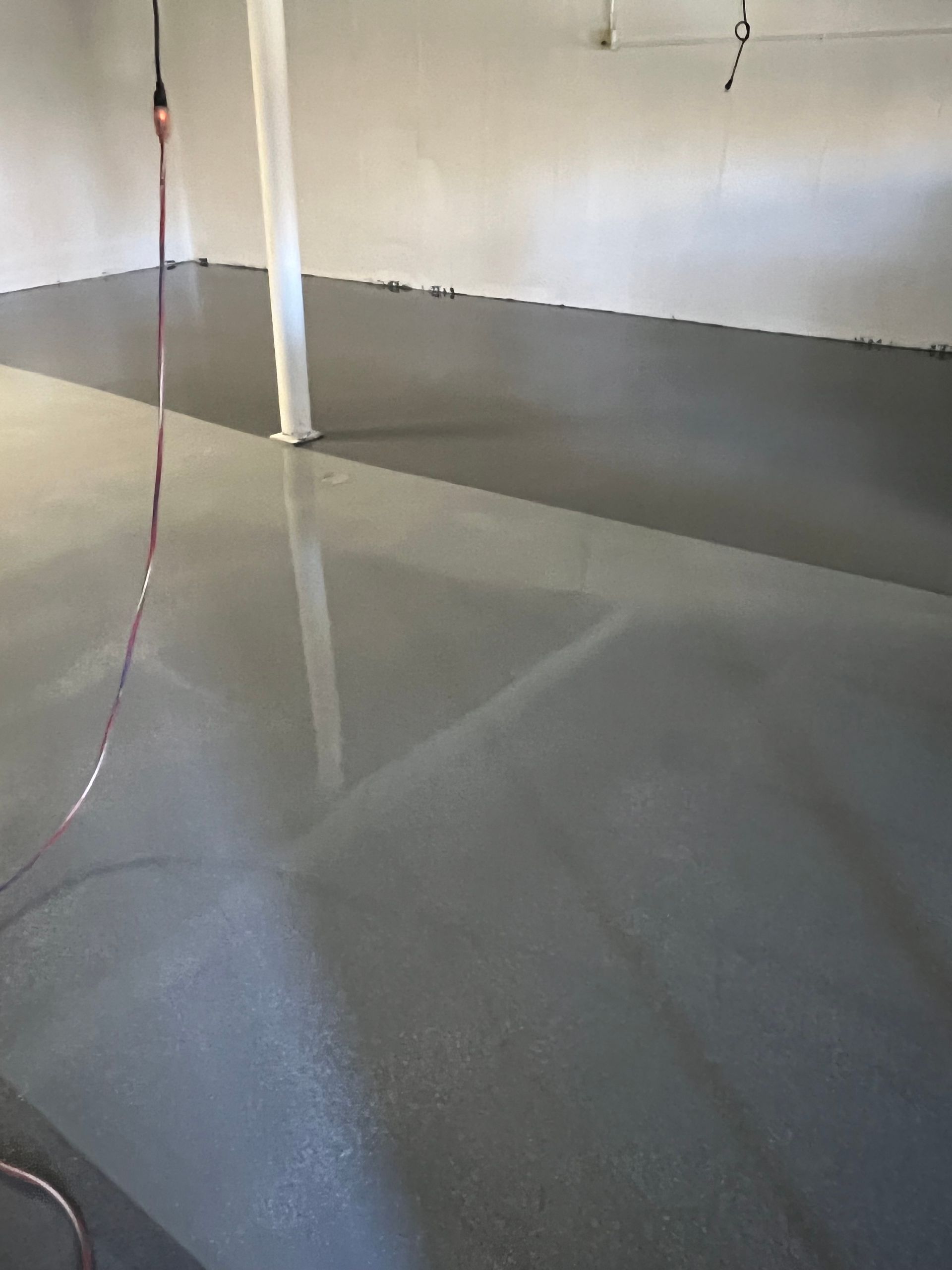Gray, glossy concrete floor in a room with white walls and a supporting column.