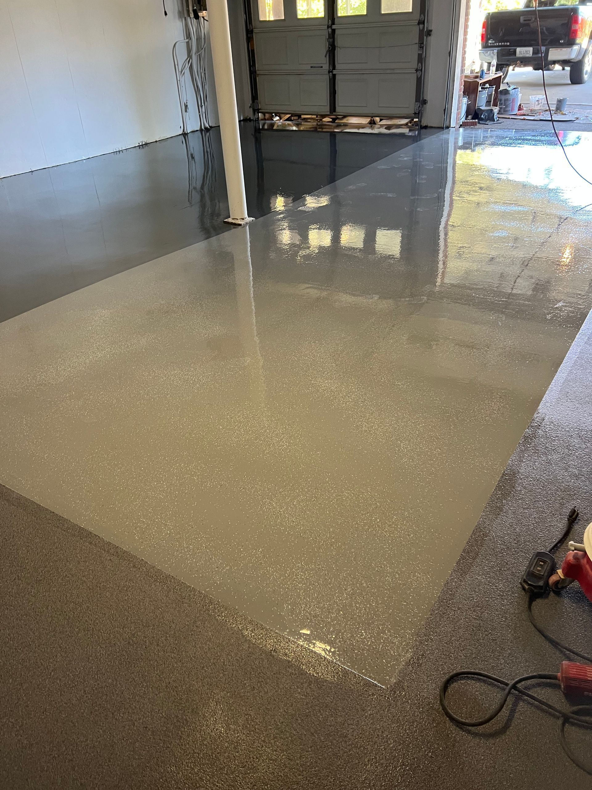 Epoxy-coated garage floor with gray and light speckled finish reflecting the open garage door.