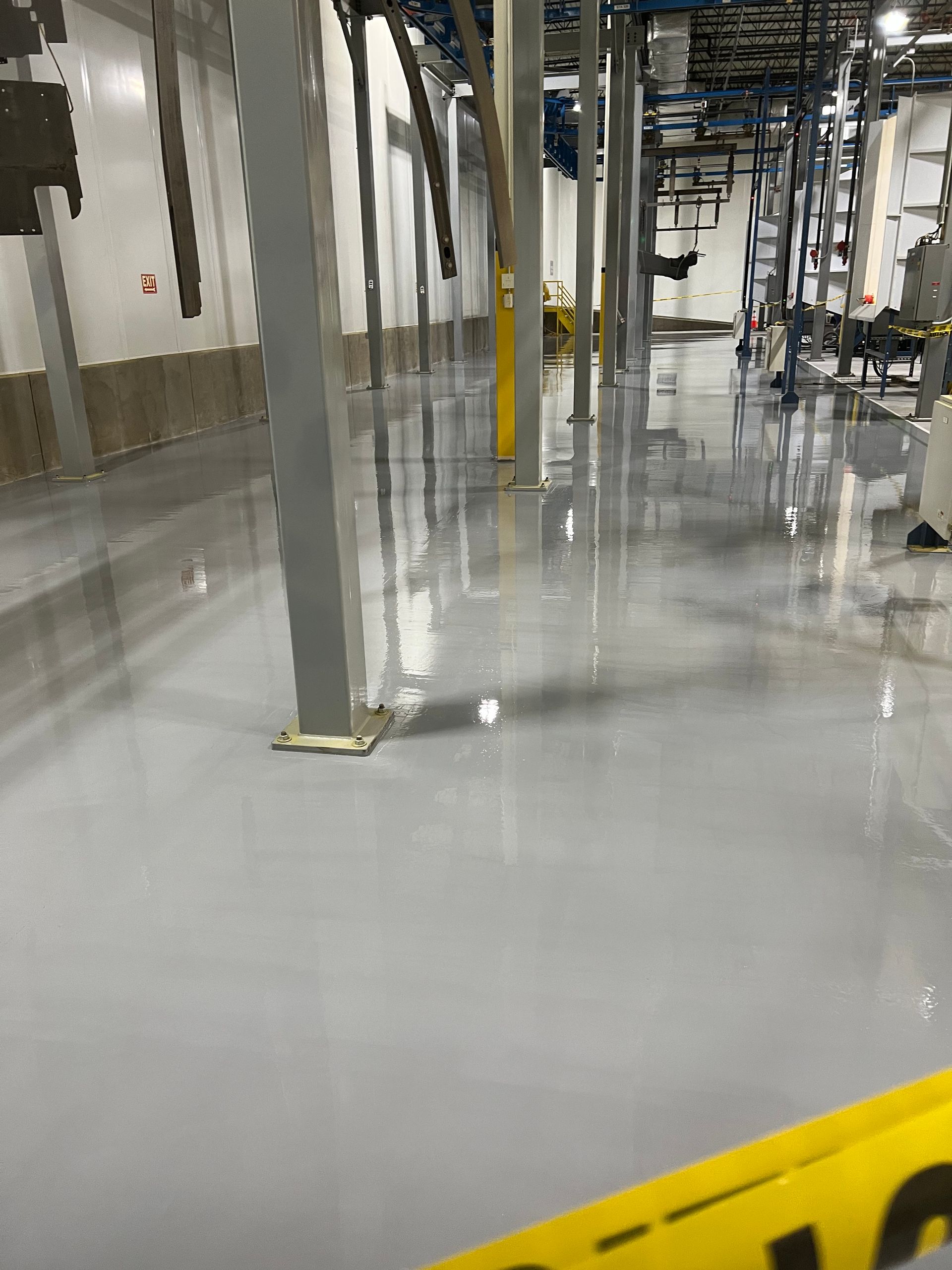Factory floor, light gray, with reflective surface, metal support beams, caution tape in the foreground.