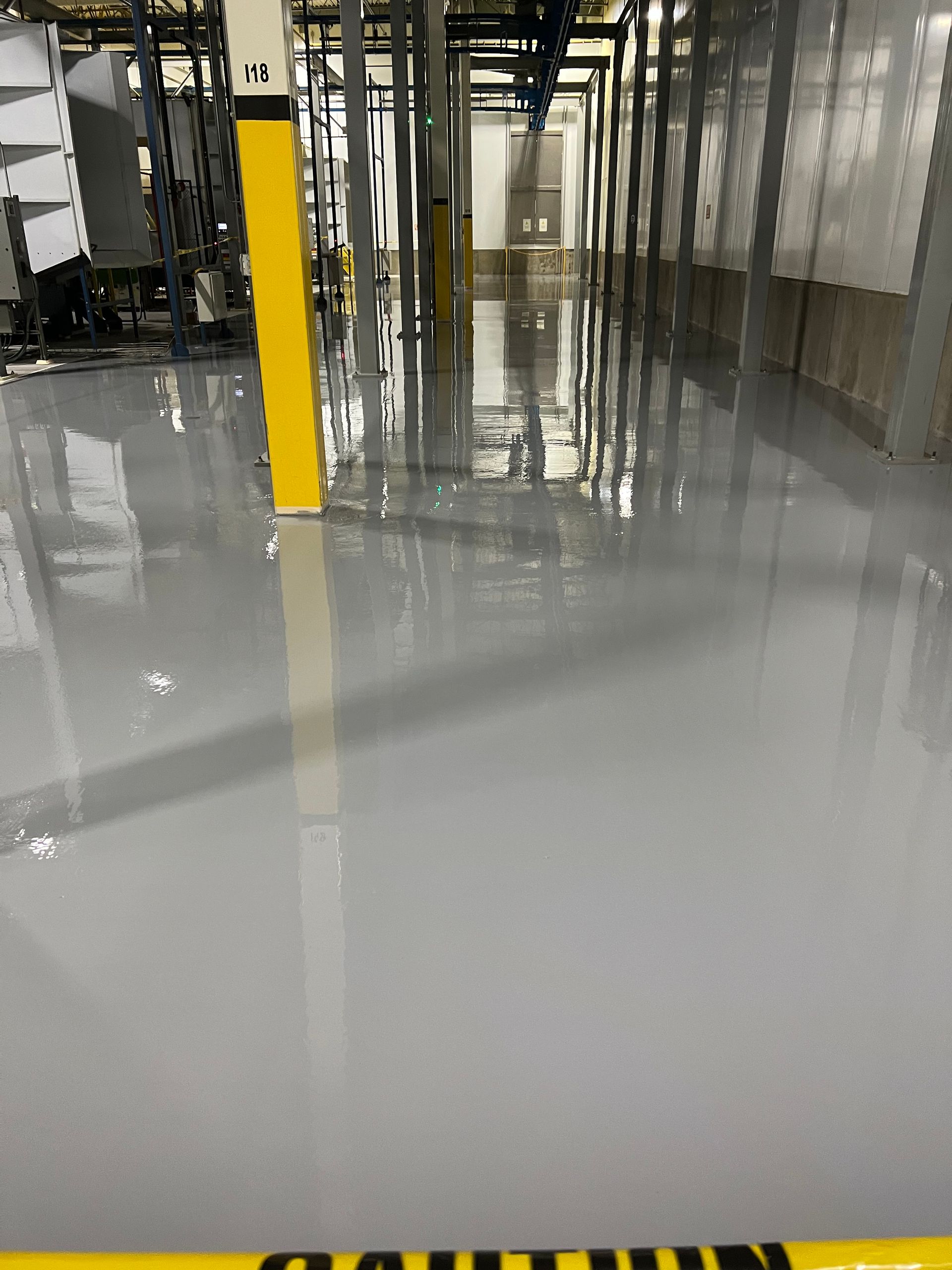 Gray industrial floor reflecting overhead equipment and a yellow caution post.