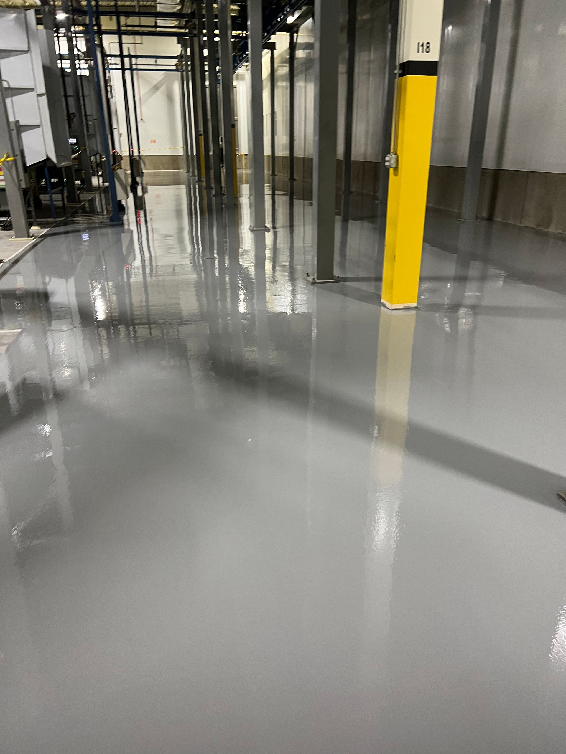 Gray epoxy floor reflecting overhead beams and equipment in an industrial setting.