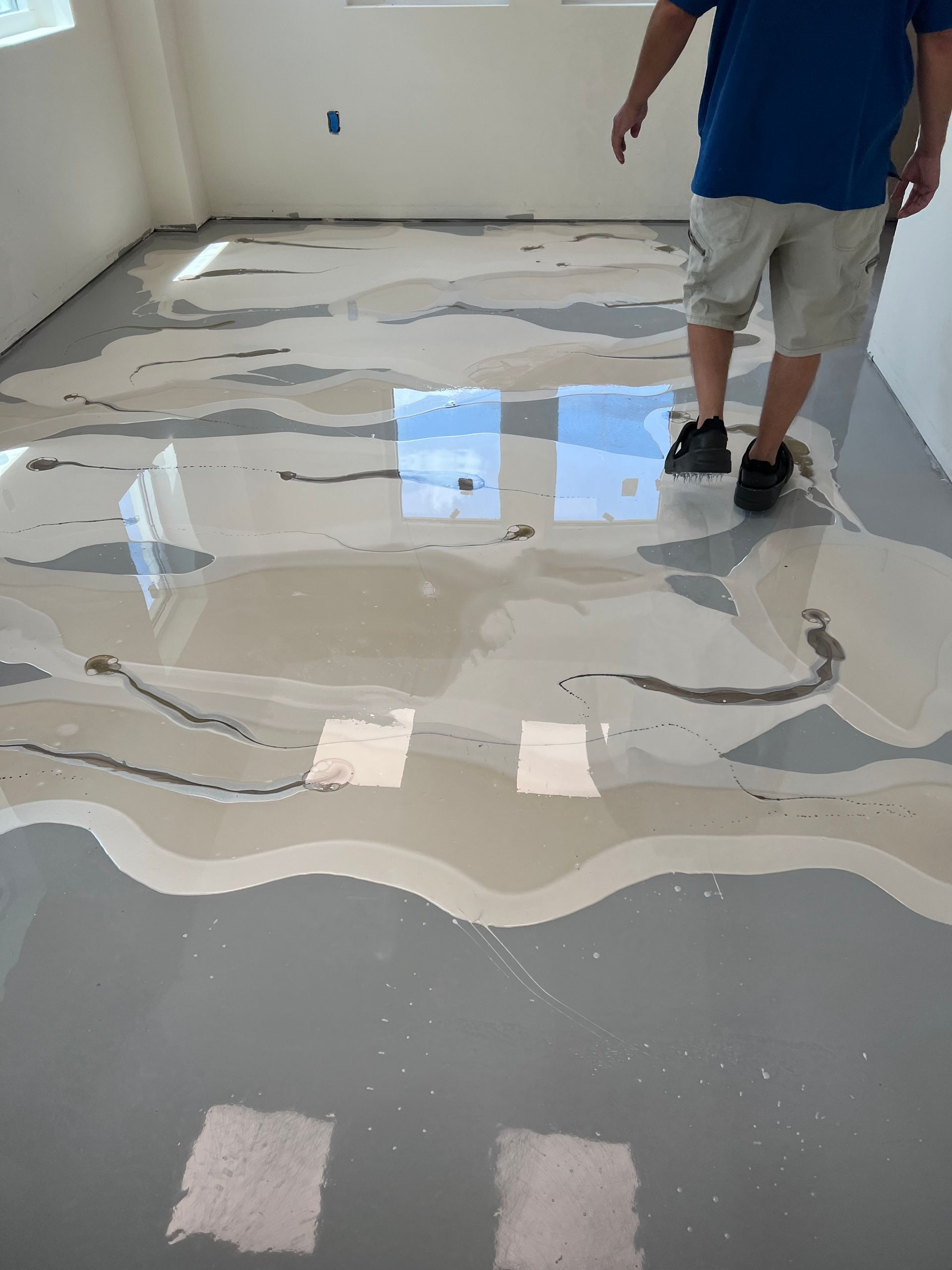 Man walks on a freshly poured, reflective epoxy floor with patches of gray and white.