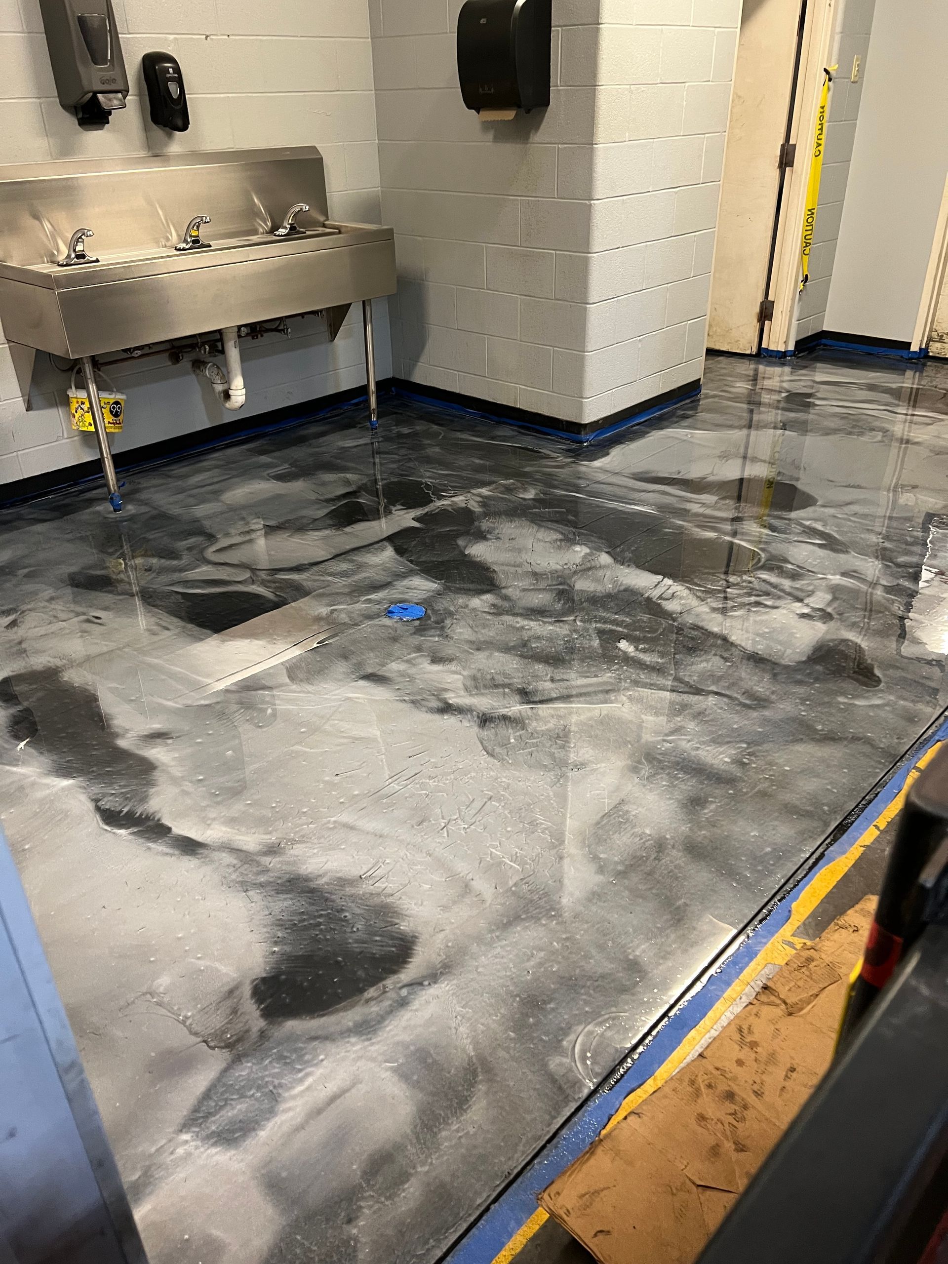 Metallic epoxy floor with a washbasin in the corner. Blue and gray swirls.