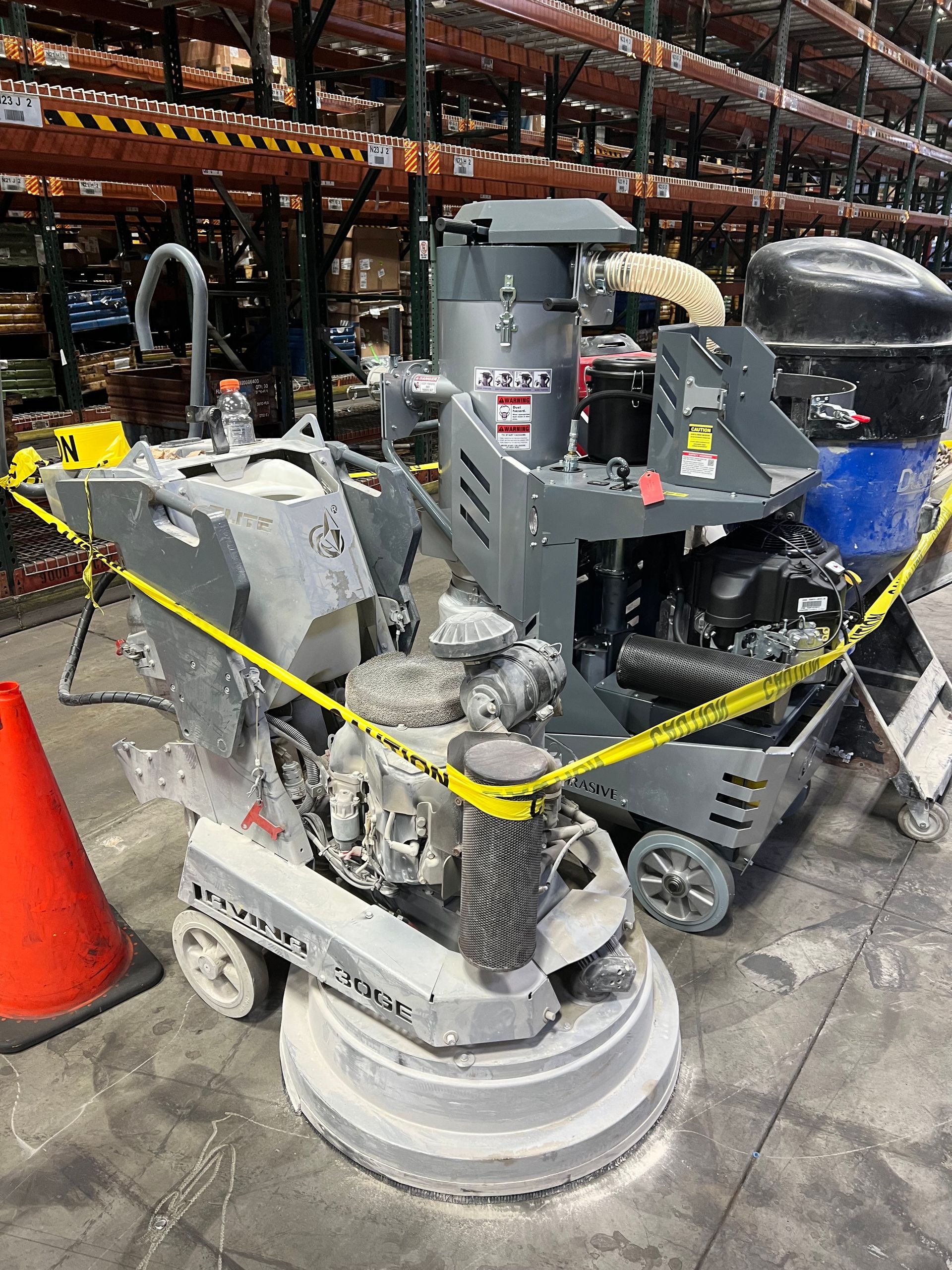 Floor grinding machines in a warehouse, cordoned off by yellow caution tape.