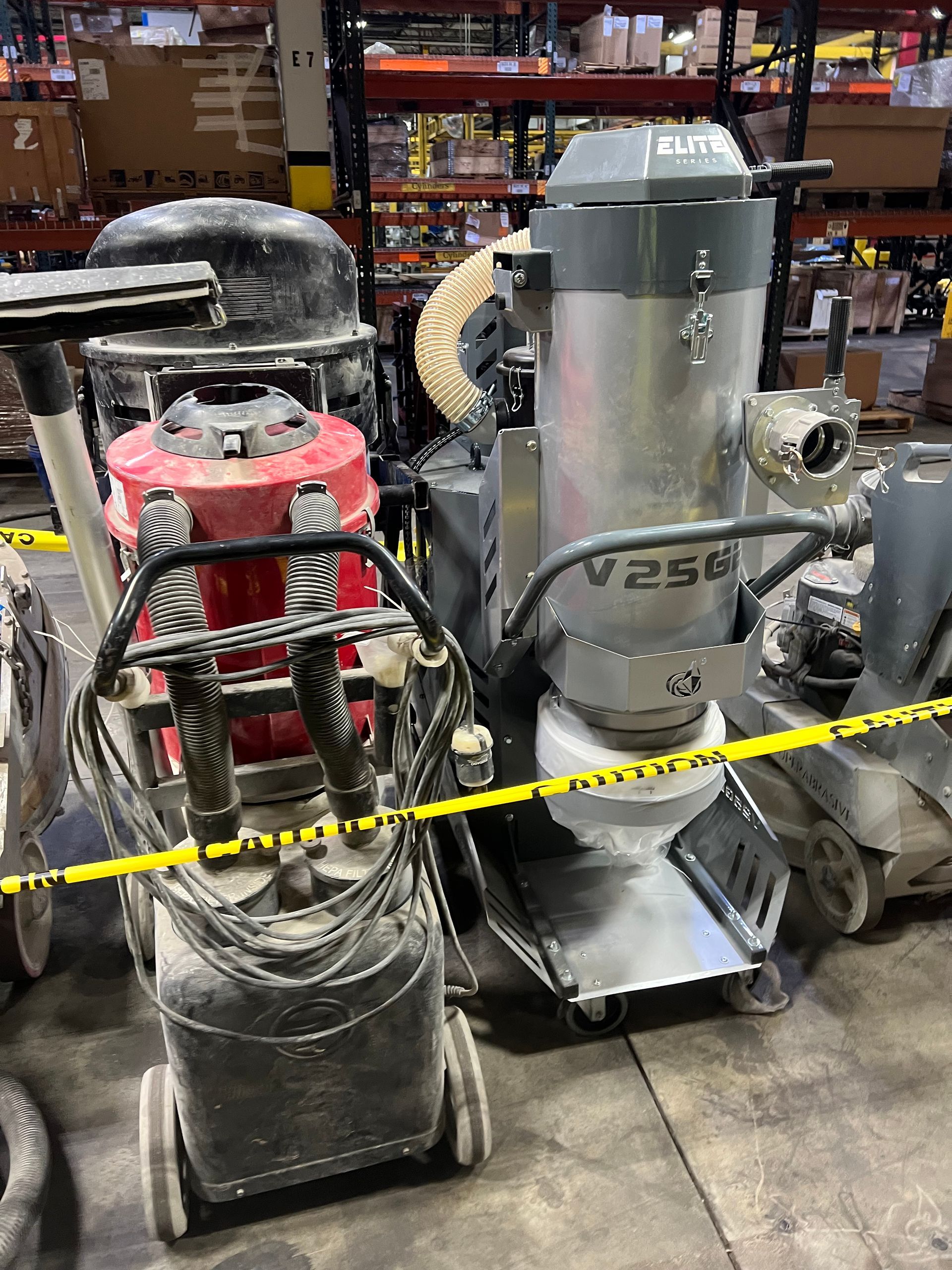 Floor grinders and dust collection vacuum on a concrete floor. Yellow caution tape in foreground.