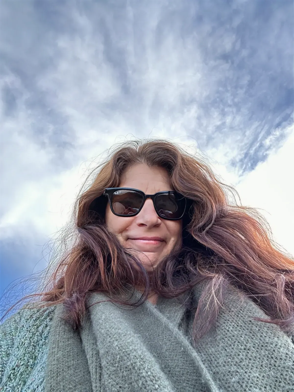 a woman wearing sunglasses and a scarf is taking a selfie .