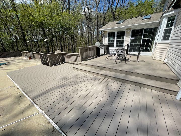 A multi-level gray composite deck attached to a house, featuring patio furniture and a grill, overlooking wooded area.