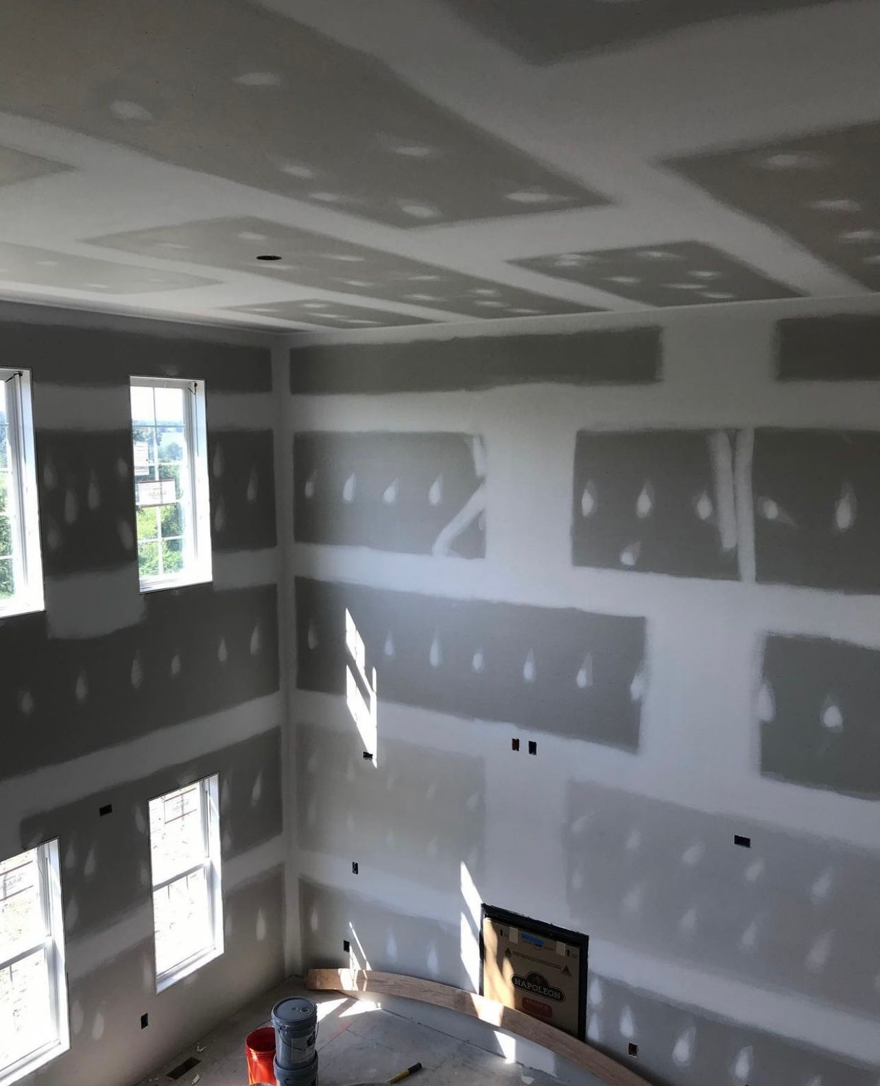 An indoor construction scene shows a room with a partial wall, caution tape, lighting tracks, and flooring materials.