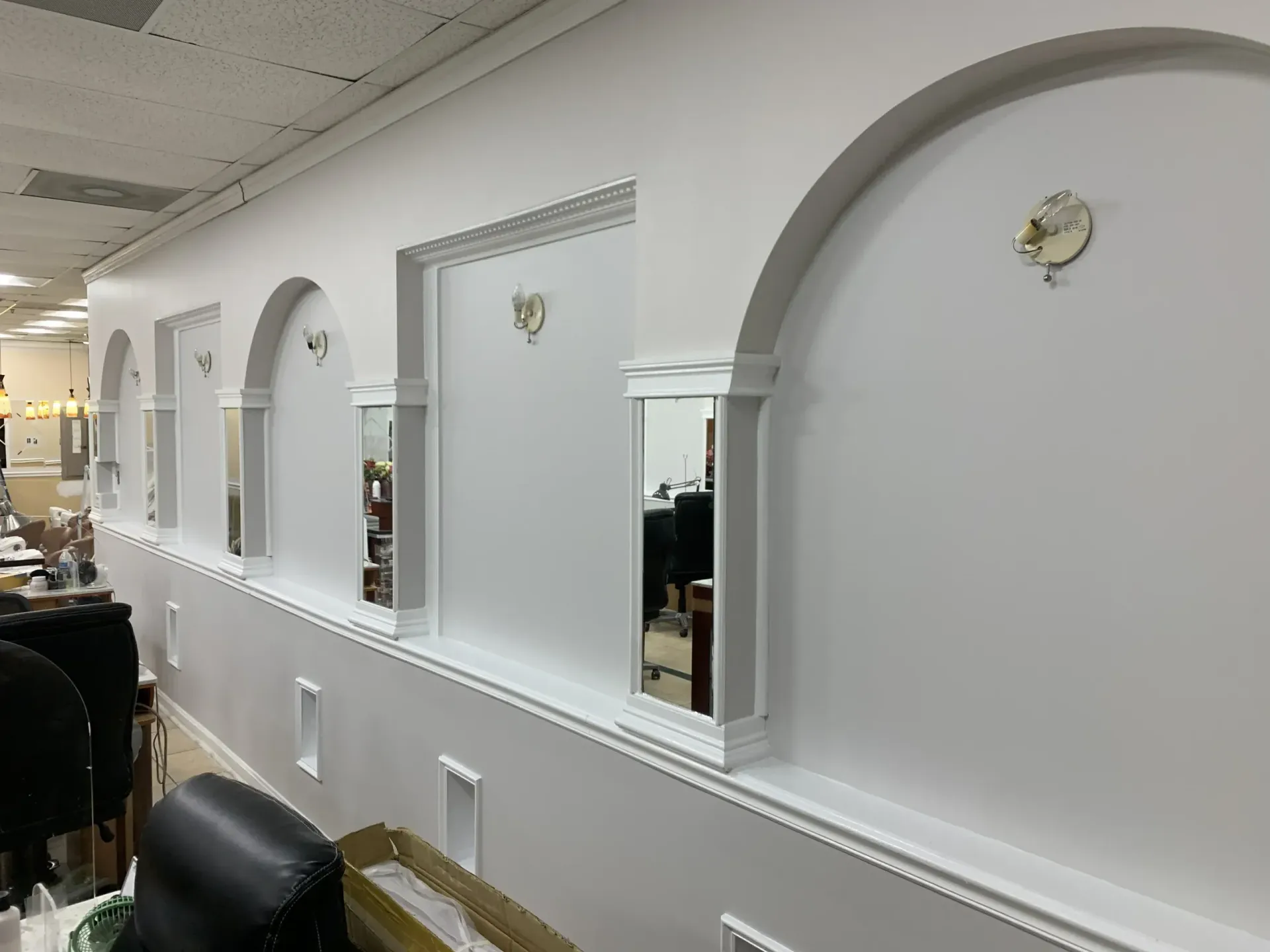 A wall in a salon featuring white arched alcoves, mirrors, and small circular light fixtures above each section.