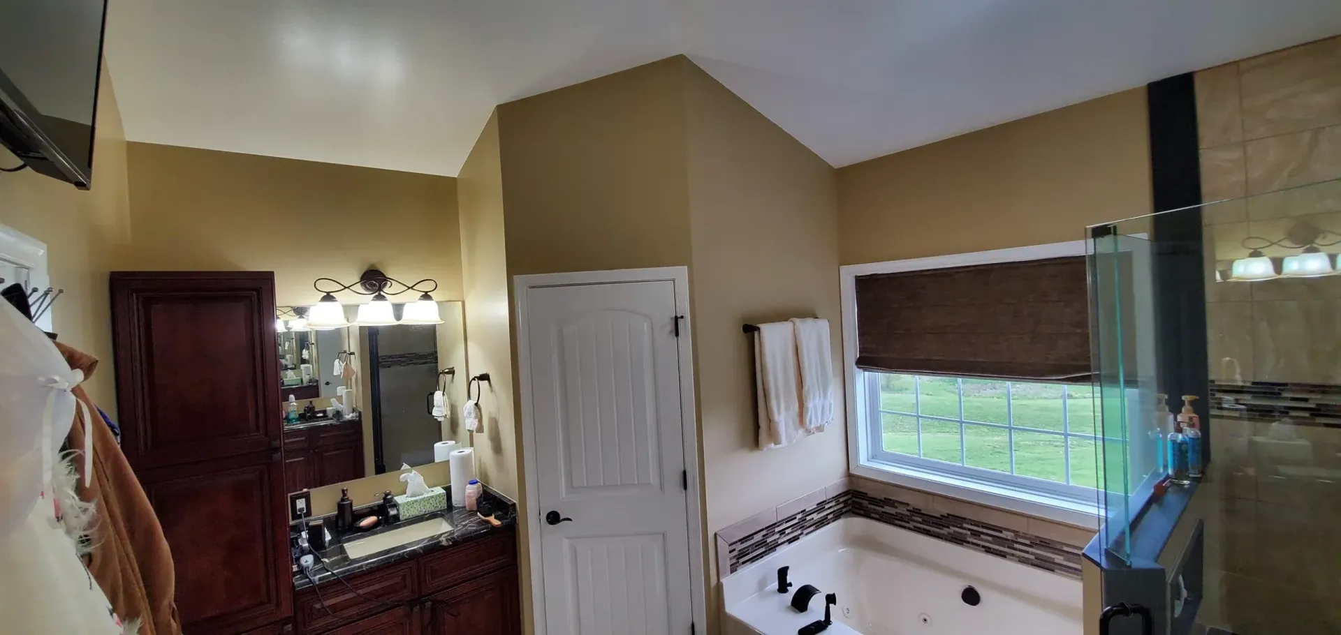 A bathroom with a dark wood vanity, a white door, and a soaking tub next to a window with a brown bamboo shade.