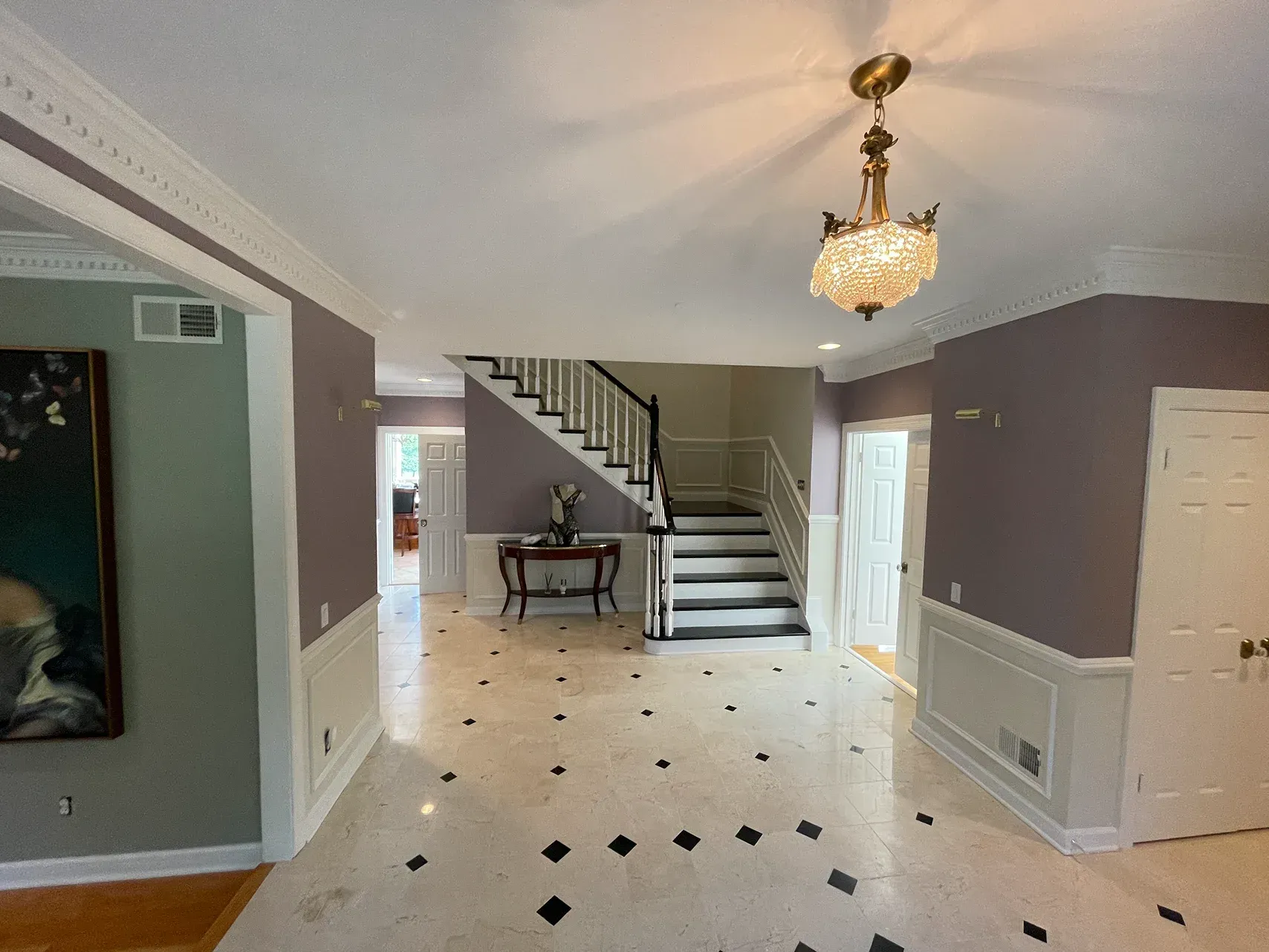 Spacious foyer with light stone floors, dark accents, a crystal chandelier, and stairs leading to an upper level.