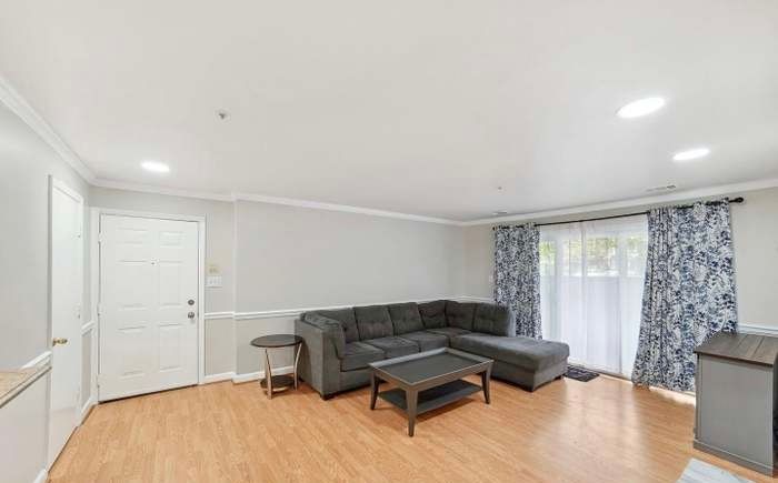 A bright living room with light wood floors, a dark gray sectional sofa, a coffee table, and floral curtains.