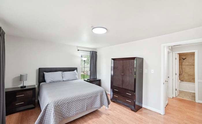 A bedroom with a queen-sized bed, dark wood furniture, and an open doorway leading to a tiled bathroom.