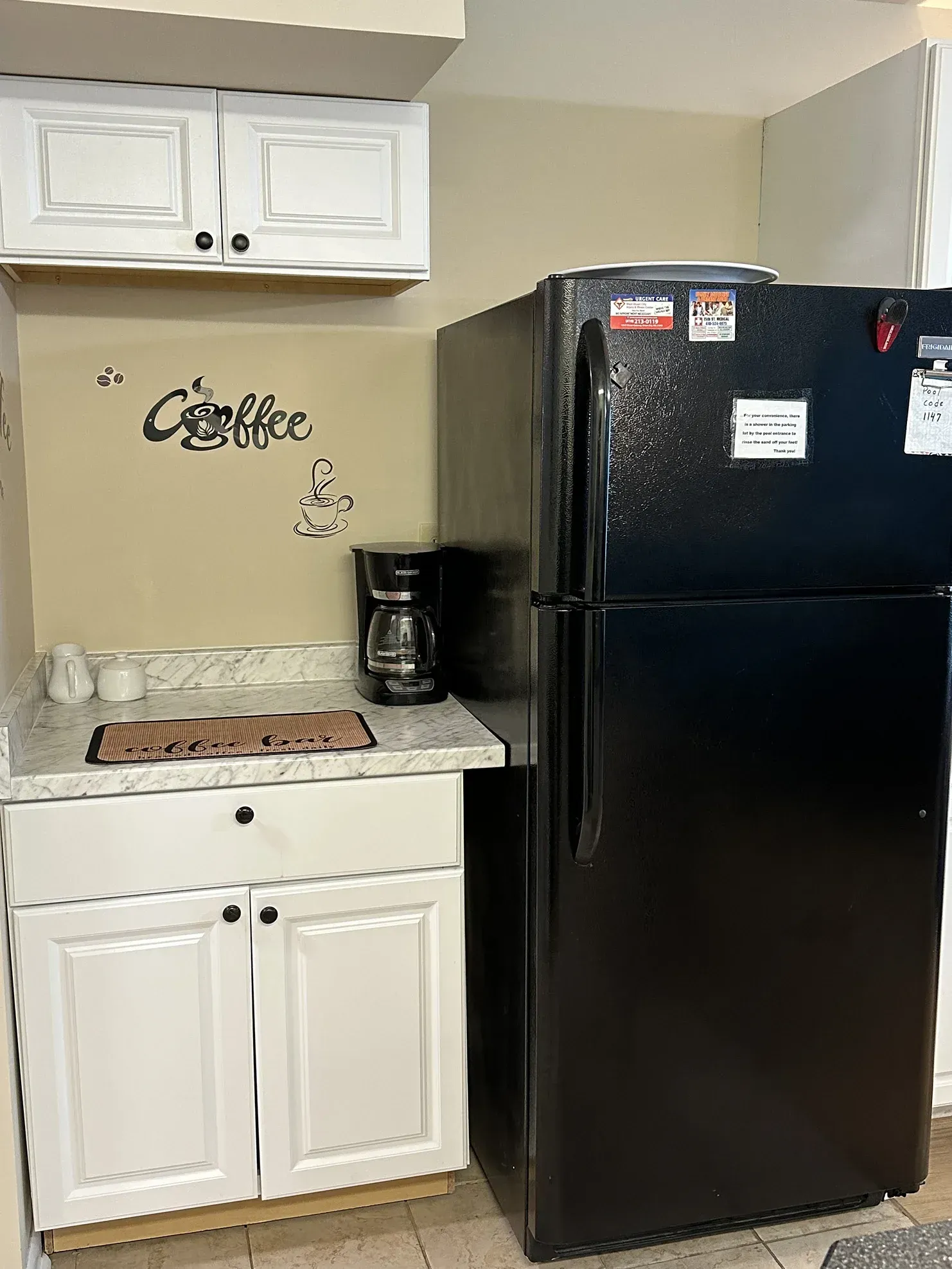 A coffee corner with white cabinets, a black refrigerator, a coffee maker, and a 