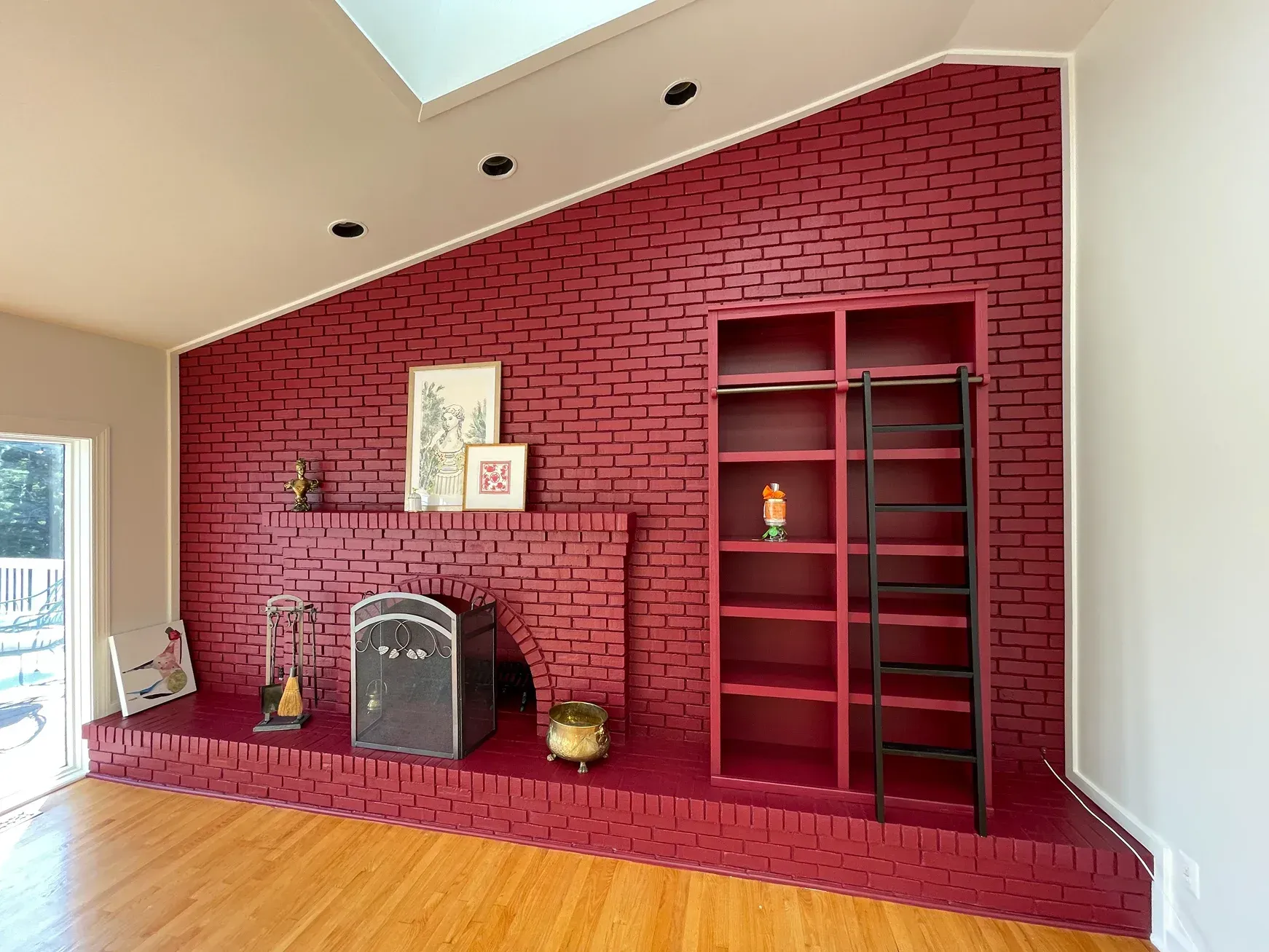 A floor-to-ceiling crimson brick fireplace with built-in shelves and a rolling black ladder against a vaulted ceiling.