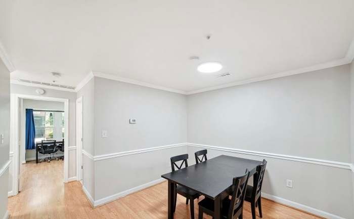 A dining room with a dark wooden table and four chairs, light gray walls with chair rail molding, and a skylight above.