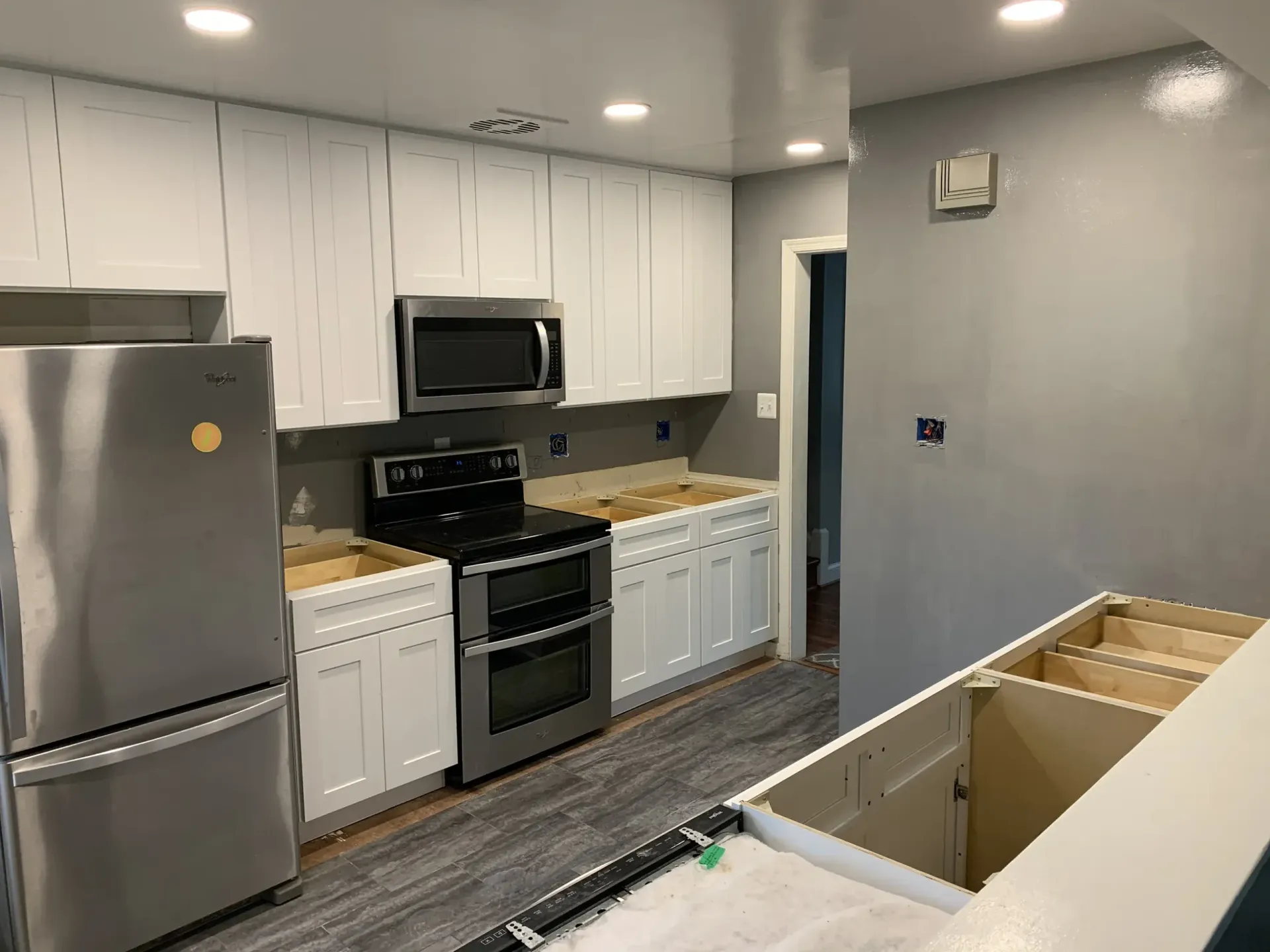 A kitchen under renovation with white cabinets, stainless steel appliances, and wood-look flooring.