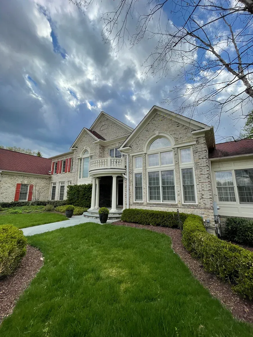A two-story stone house with a red roof, front pillars, and arched windows under a cloudy, dramatic sky.
