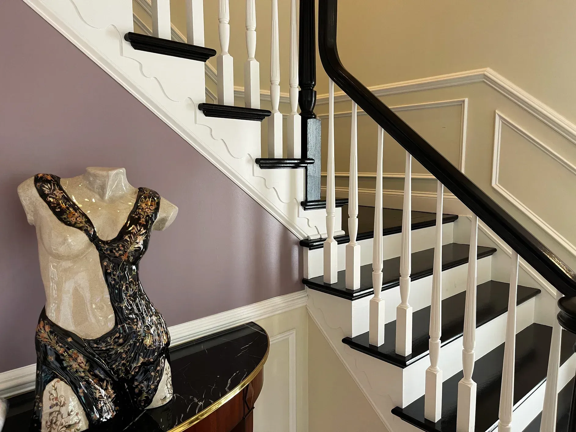 A white and black staircase next to a mannequin torso draped in a decorative black garment on a curved wooden table.