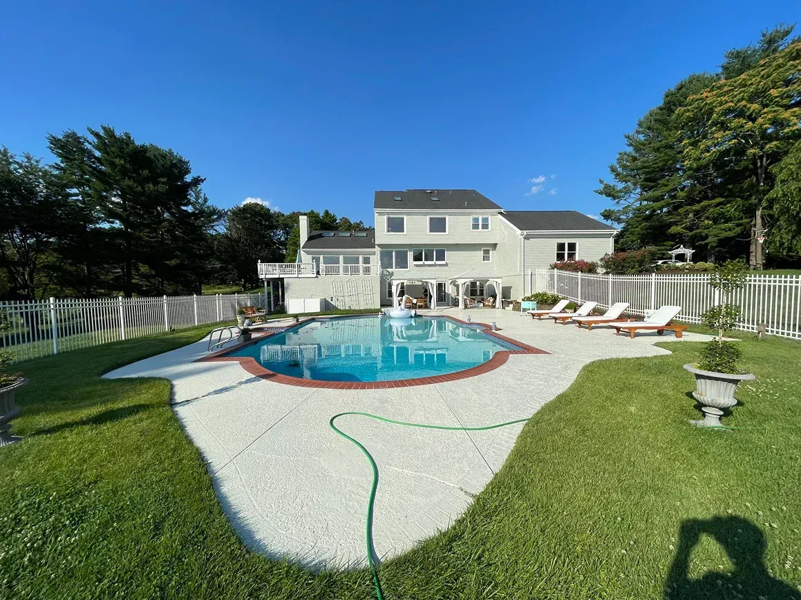 A light-colored two-story house with a backyard swimming pool surrounded by a white gravel patio and green lawn.