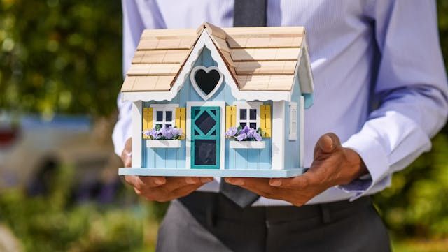 a person holding a house figurine outside