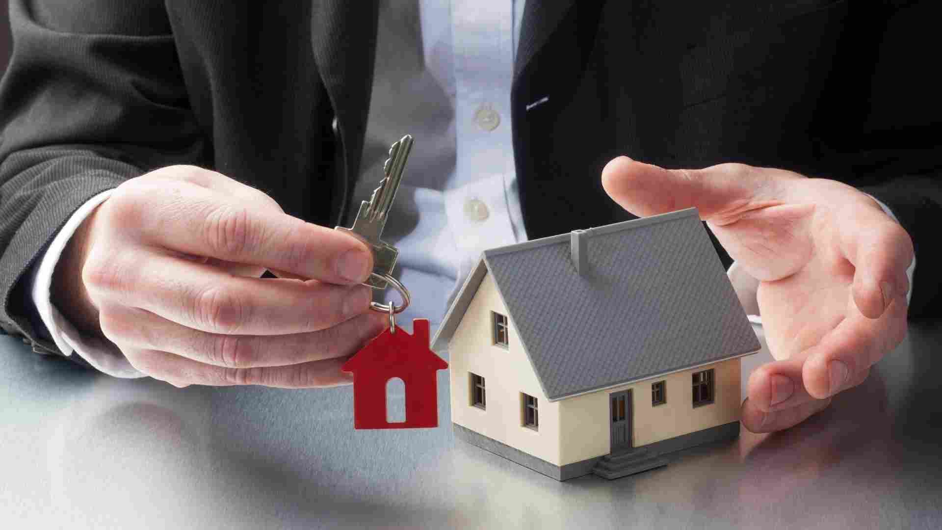 a person holding a house key next to a small home figurine