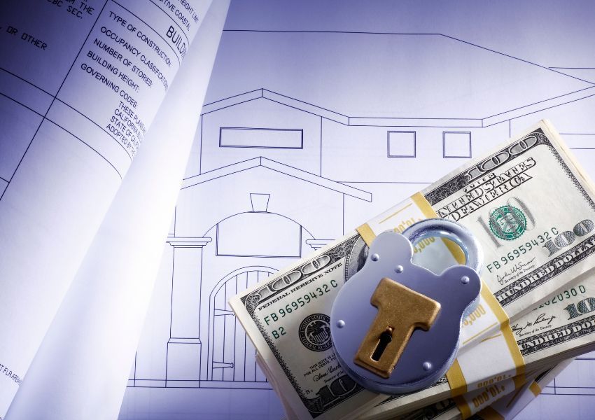 a stack of one hundred dollar bills and a lock on top of a homes blue print