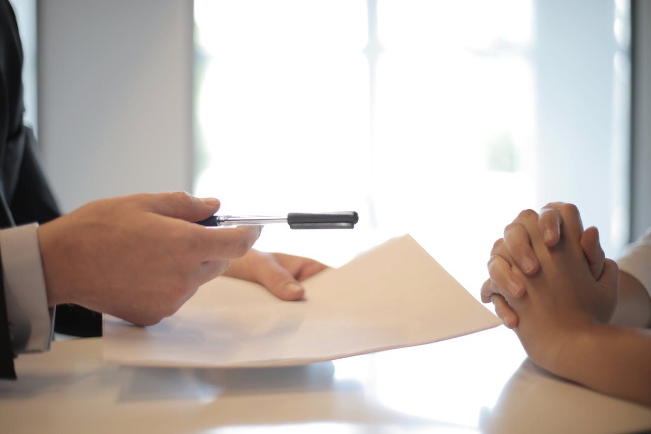 person holding pen and paper and person with hands crossed