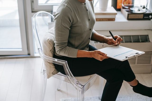person in a grey sweater filling out a questionnaire on a clipboard