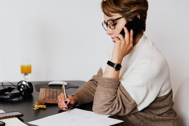 person on the phone while taking notes on a white piece of paper