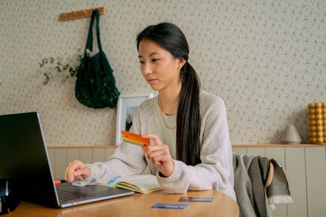 person sitting at their kitchen table making an online rent payment whole holding an orange credit card