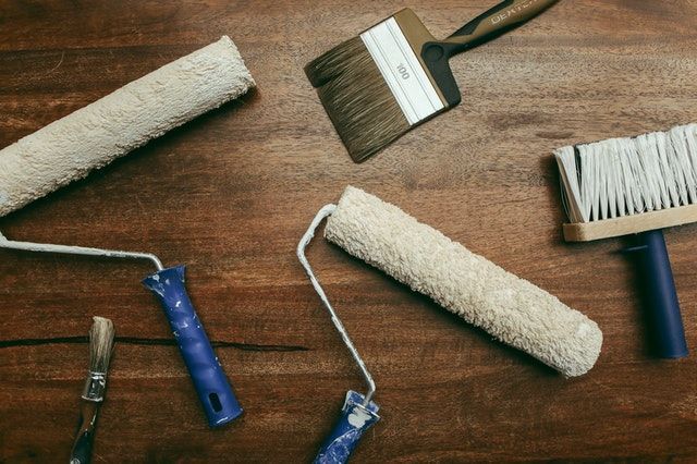 two clean paint rollers and and two wide paint brushes on a dark wood floor