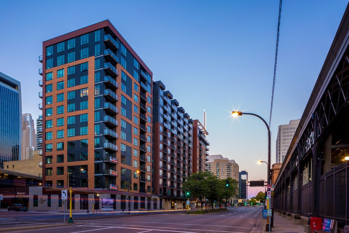 Tall apartment building on a city street at dusk; brown and blue facade, streetlights, clear sky.