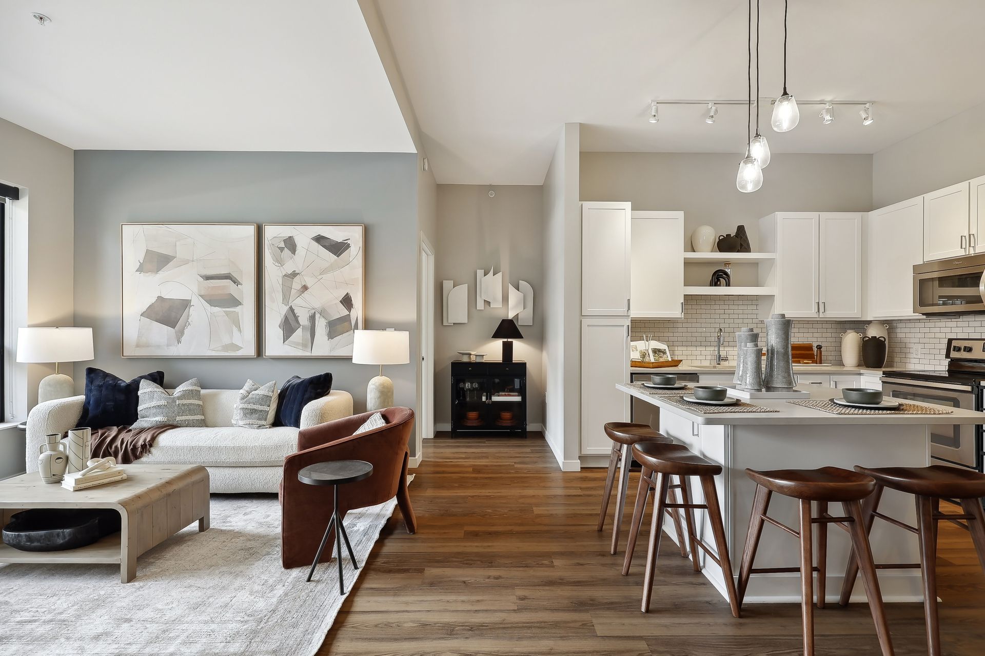 Open-concept apartment living space: living room with sofa, kitchen with island, wooden floors, and neutral colors.