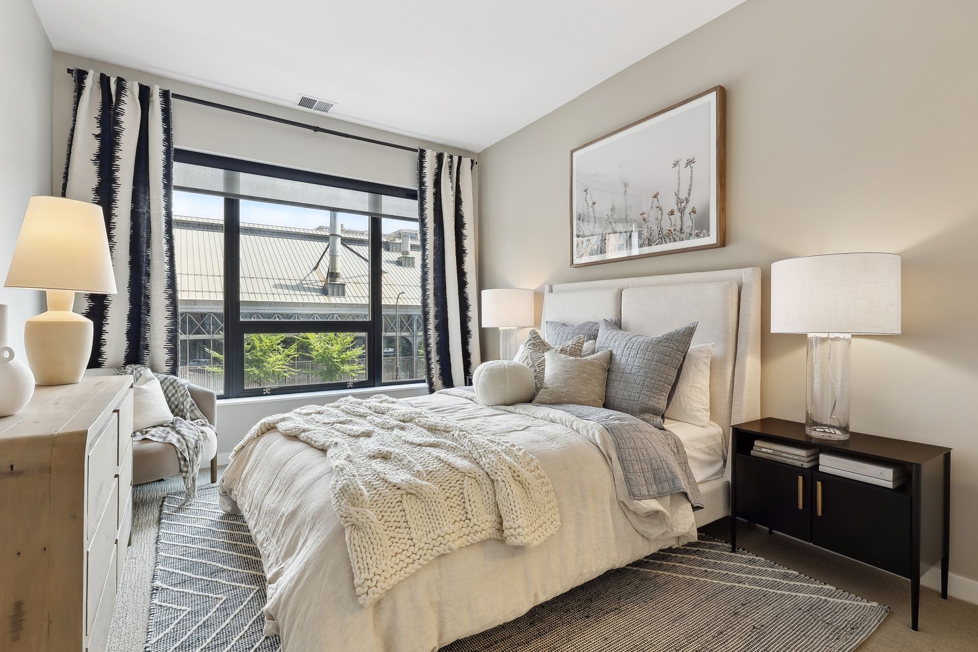 Bedroom with bed, nightstands, window with curtains, and artwork. Neutral colors with blue accents.