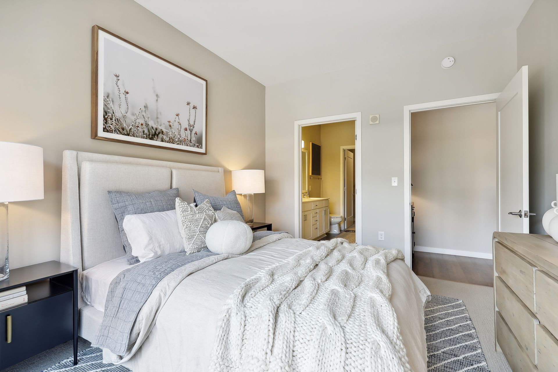 Bedroom with a bed, nightstands, art, and bathroom doorway. Neutral tones, cozy bedding, and modern decor.