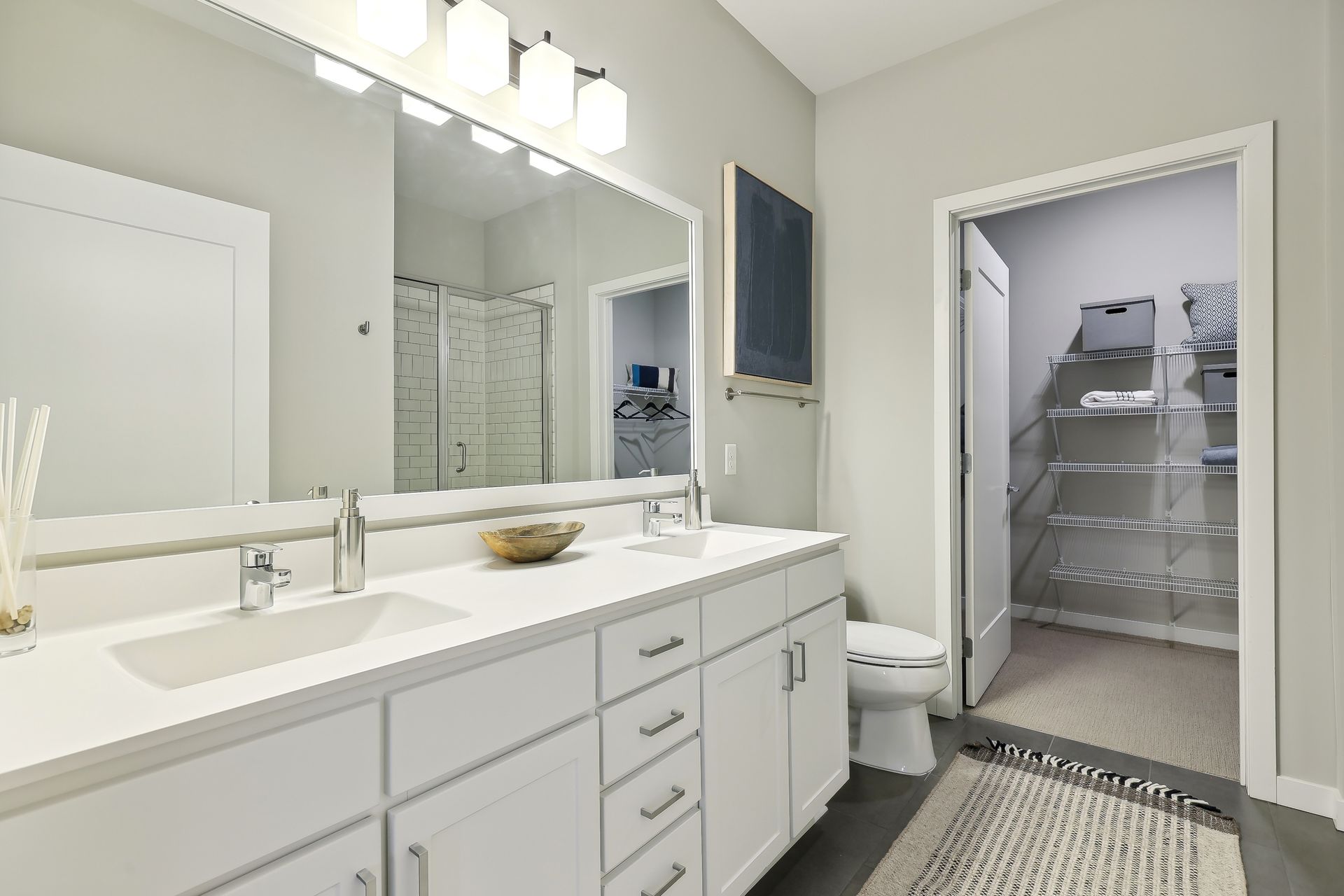 Bathroom with white vanity, double sinks, and open doorway to a walk-in closet.