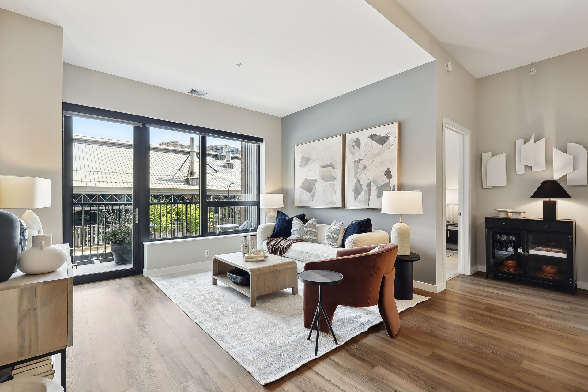 Modern living room with large windows, light blue walls, and hardwood floors.