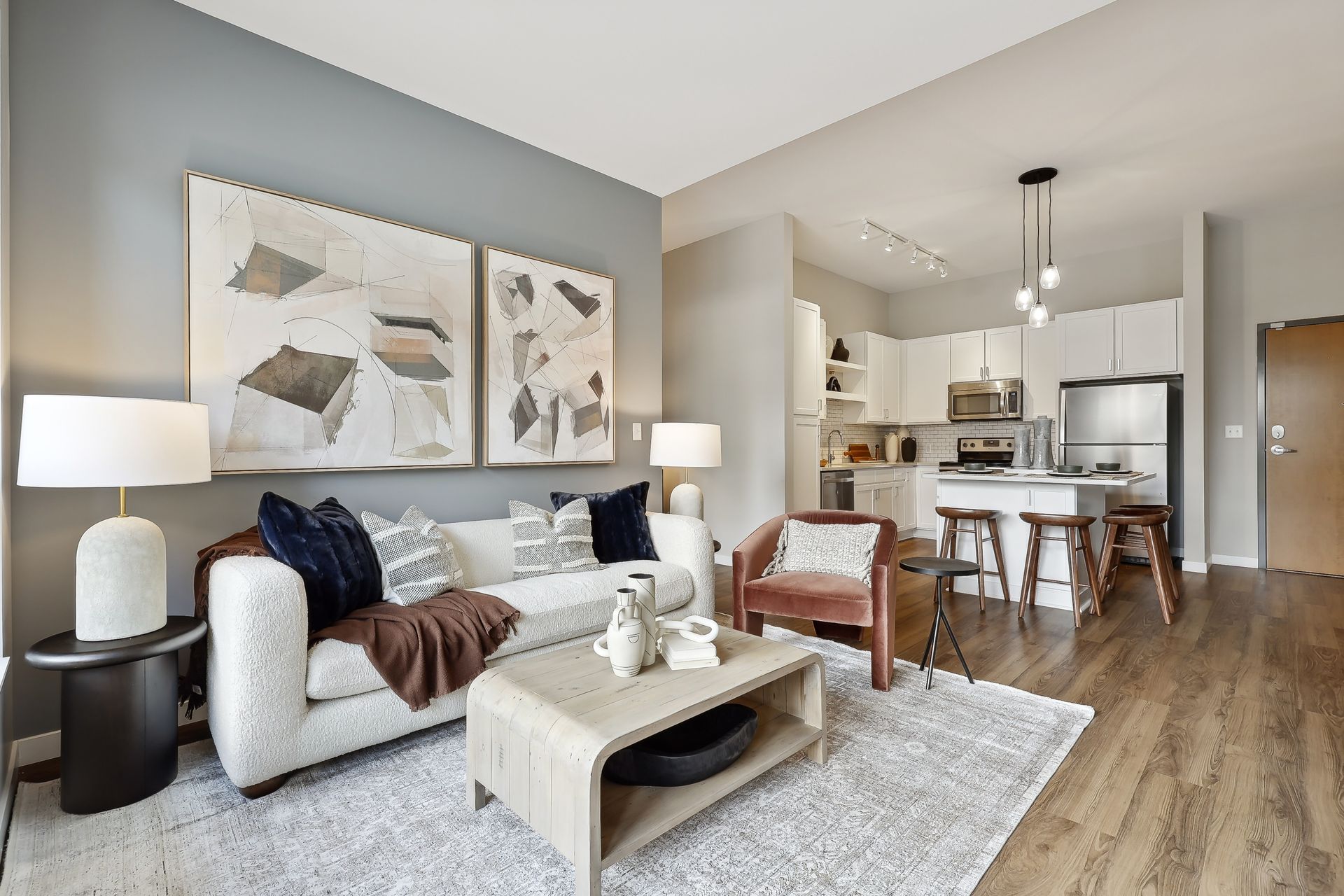 Living room with open kitchen, modern decor. White couch, gray walls, wooden floors.