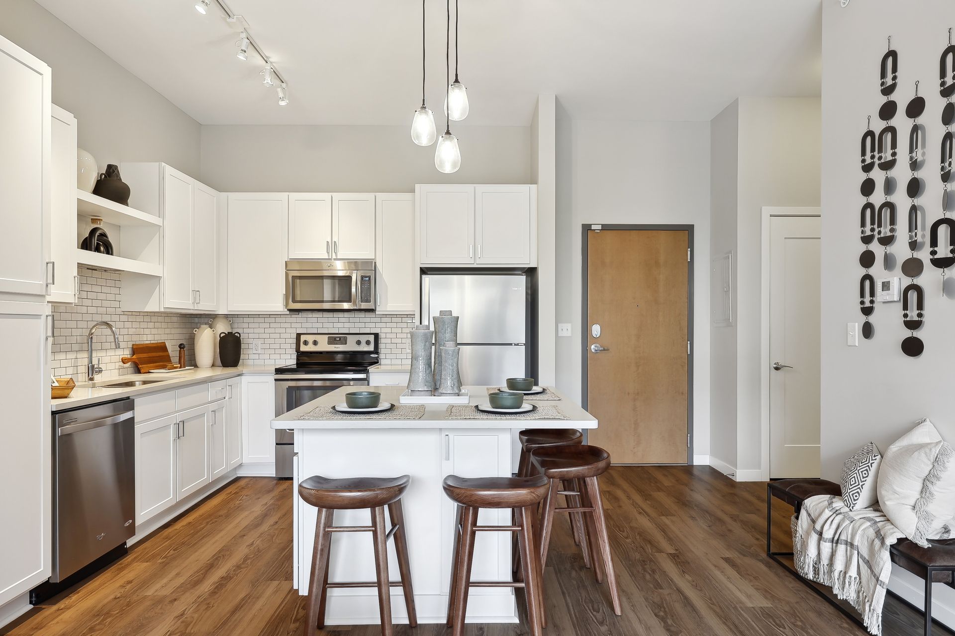 Modern white kitchen with island seating and stainless steel appliances, wood floors.