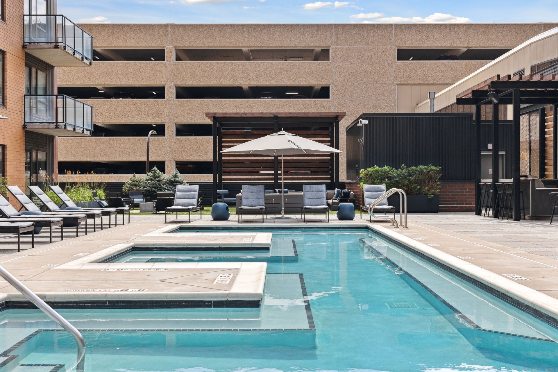 Pool area with lounge chairs, a shaded seating area, and a parking garage in the background.