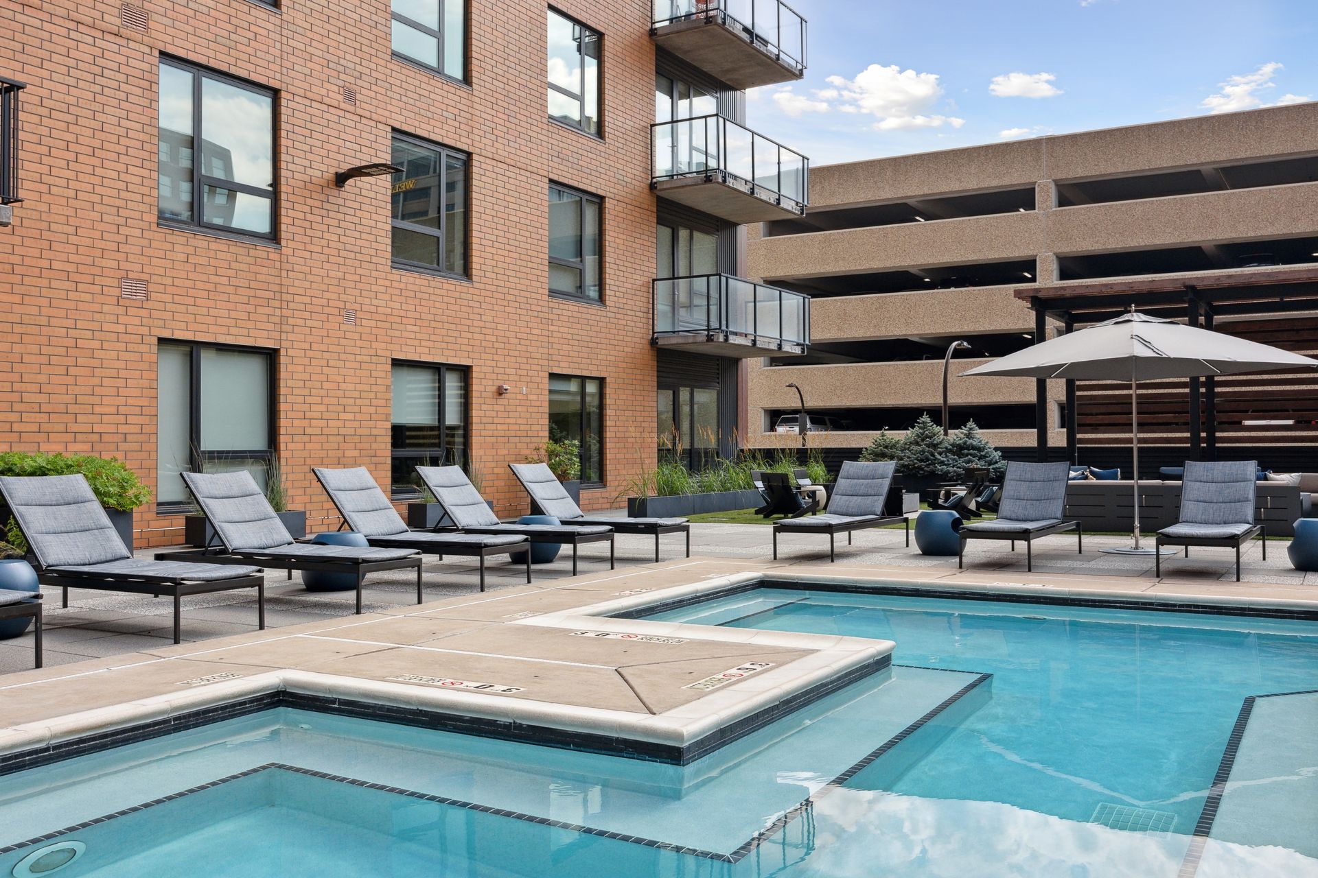 Pool area with lounge chairs, umbrella, and brick apartment building.