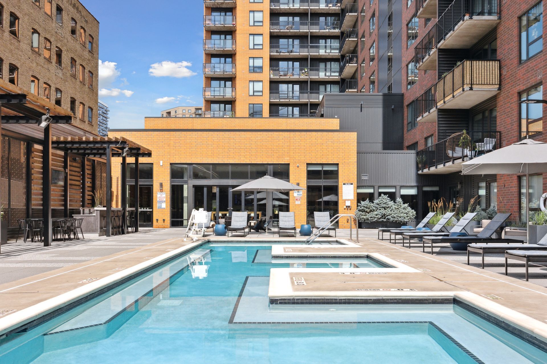 Pool area with loungers, umbrellas, and a large building in the background.