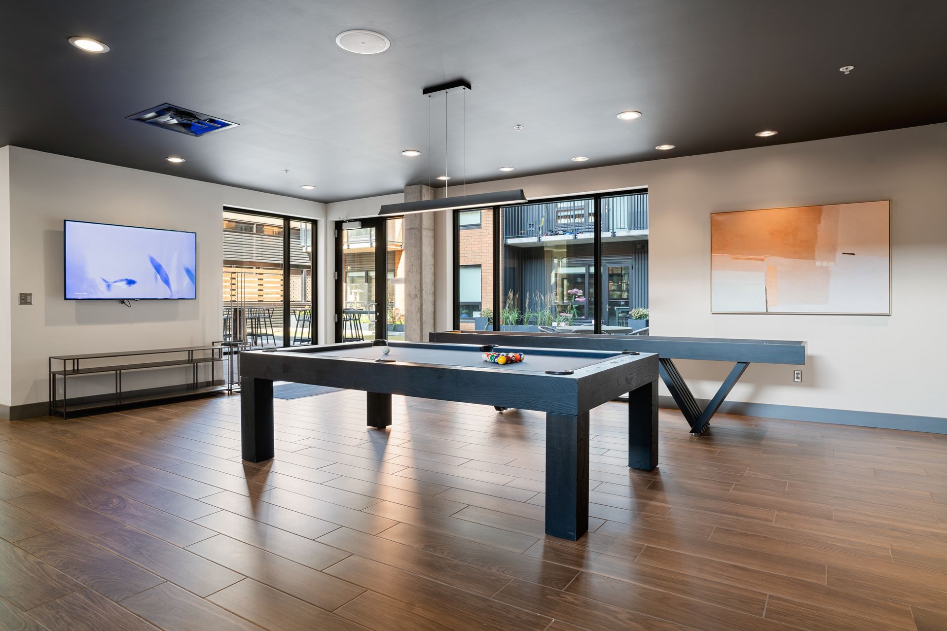 Game room with pool table, ping pong table, and TV. Wooden floors and large windows.