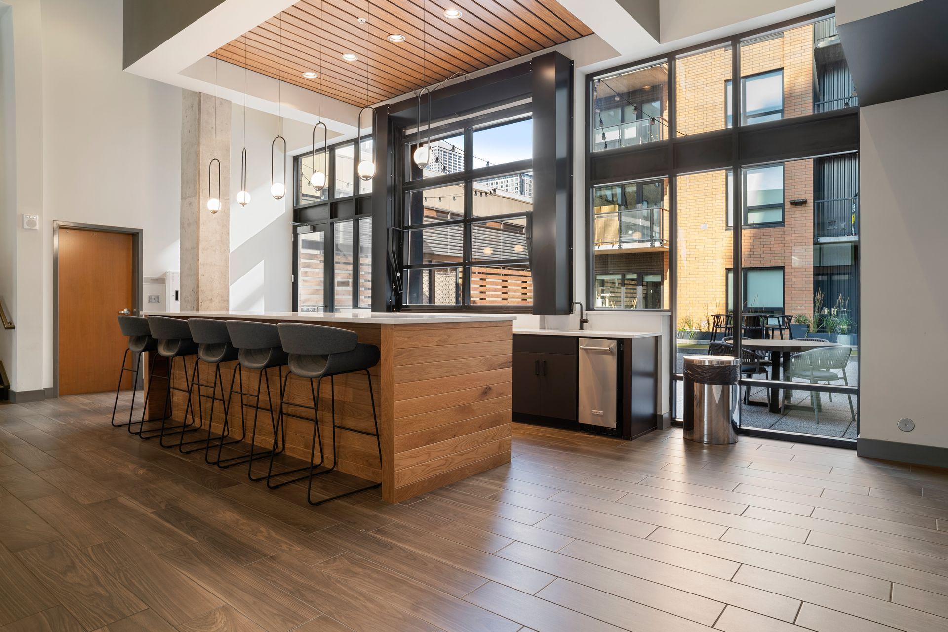 Modern kitchen with wood island, stools, and floor-to-ceiling windows overlooking an outdoor patio.