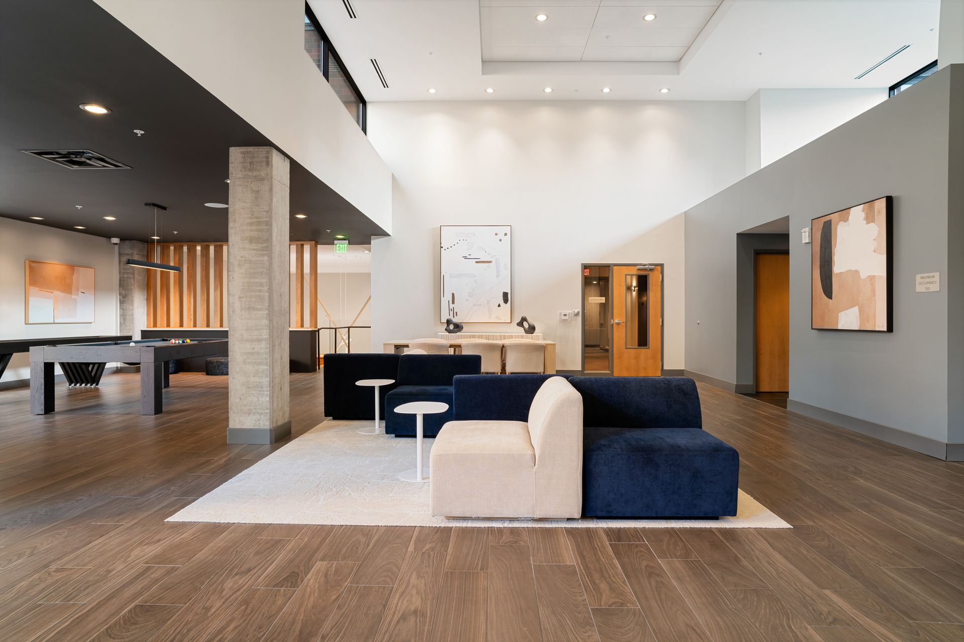 Spacious modern lobby with seating, pool table, artwork, and wood flooring. Navy and white sofa.
